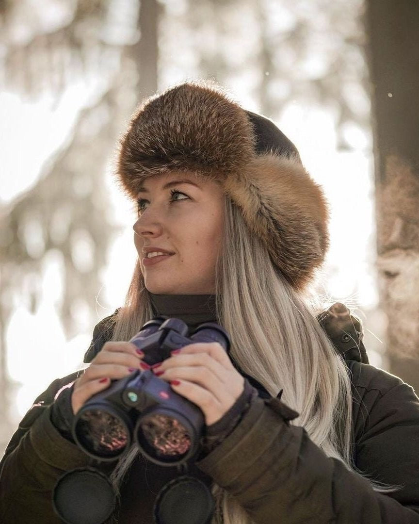 Frau mit Rotfuchsmütze und Fernglas im Winterwald