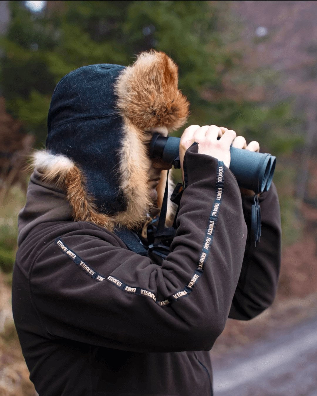 Person mit Rotfuchsmütze blickt durch ein Fernglas